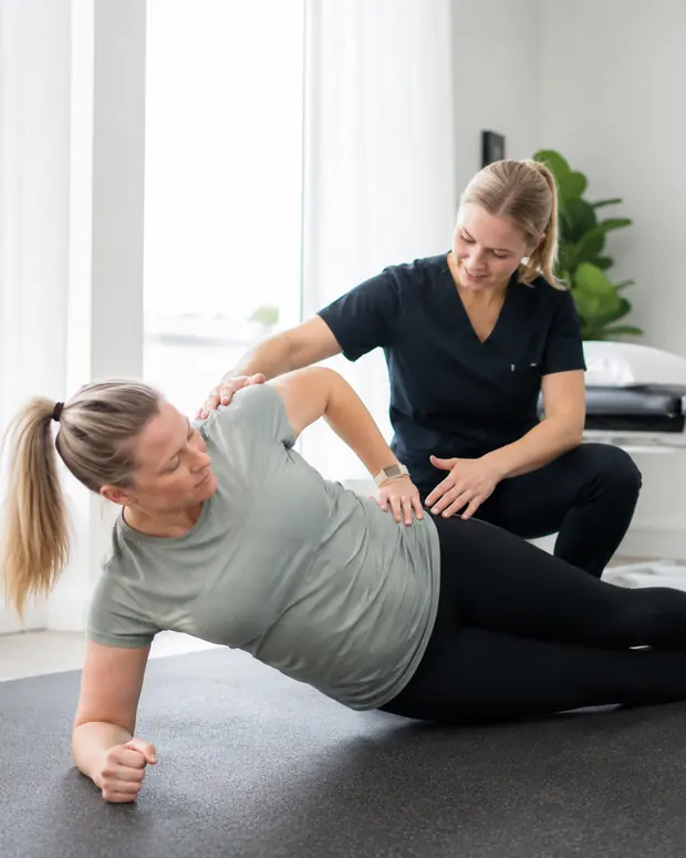 A physiotherapist guiding a client through an exercise on the floor of the practice.